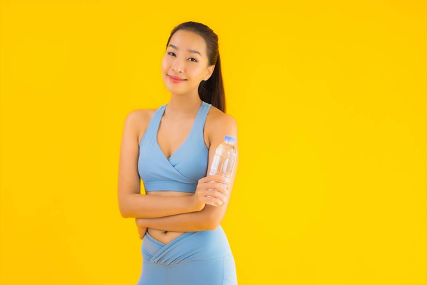 Portrait beautiful young asian woman with bottle water on yellow isolated background - Photo, Image