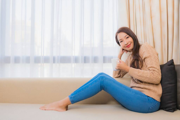 Muotokuva kaunis nuori aasialainen nainen kahvikuppi sohvalla sisustus sisätilojen olohuone - Valokuva, kuva