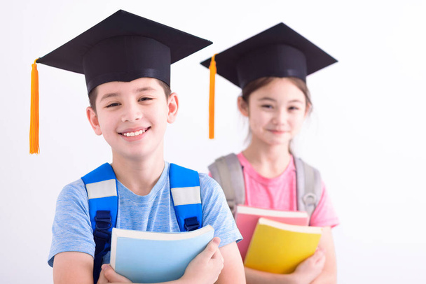 Feliz niño y niña en la gorra de graduación sosteniendo libros - Foto, imagen