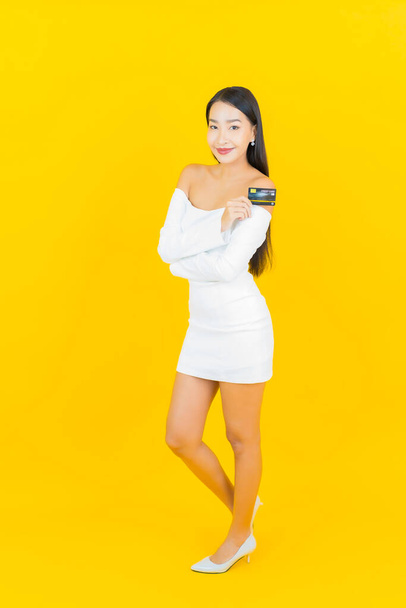 Portret mooie jonge business aziatische vrouw met slimme mobiele telefoon en creditcard op gele achtergrond - Foto, afbeelding