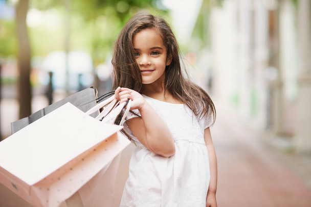 Forget playtime - I want to shop all day. Portrait of an adorable little girl holding shopping bags while out in the city. - Фото, изображение