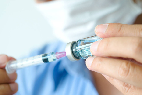De hand van de dokter houdt een spuit en een blauwe fles vaccin vast in het ziekenhuis. Gezondheids- en medische begrippen - Foto, afbeelding