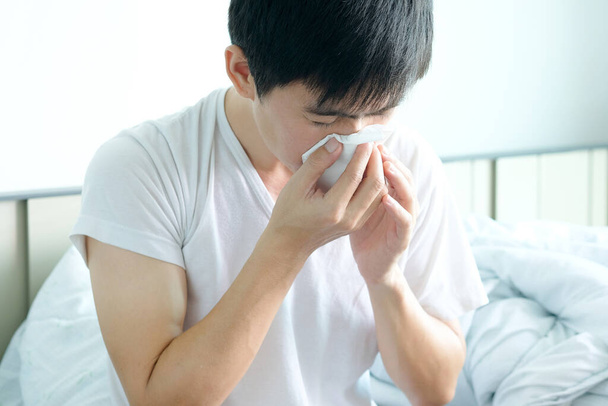 Sick man is flu, using a paper napkin and he have a runny nose. And he was covered in warm cloth.Health concept - Фото, изображение