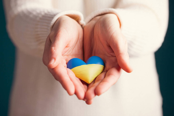 Heart shaped flag of Ukraine in female hands. The concept of solidarity with the citizens of Ukraine. - Photo, Image