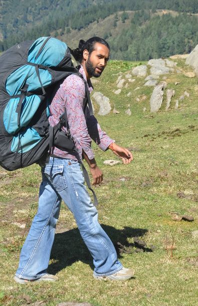 Vista lateral de um viajante masculino olhando para a câmera enquanto caminha na montanha com mochila de paraquedas - Foto, Imagem