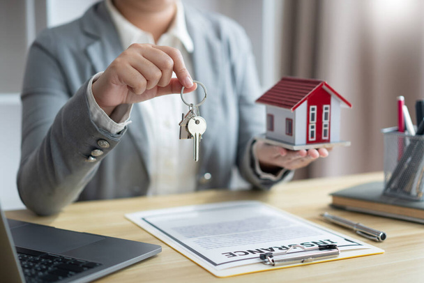 Koncepcja ubezpieczenia przedstawiciel nieruchomości trzymający klucz do domu po prawej stronie i model domu po lewej stronie. - Zdjęcie, obraz