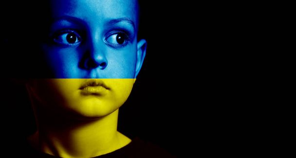 Μικρό αγόρι ζωγραφισμένο σε χρώματα της ουκρανικής σημαίας σε μαύρο φόντο. Σταματήστε τον πόλεμο. - Φωτογραφία, εικόνα