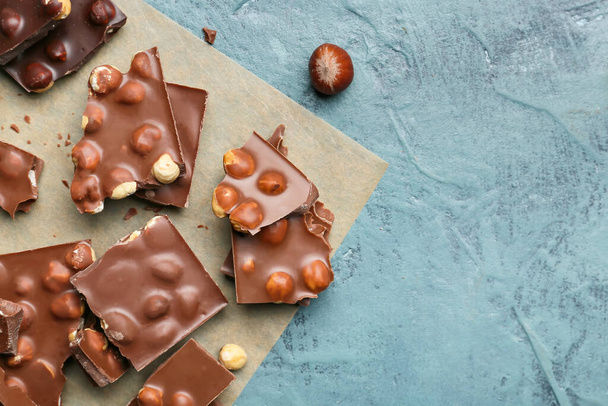 Stücke leckere Schokolade mit Nüssen auf farbigem Hintergrund - Foto, Bild