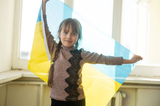 Ένα μικρό κορίτσι με μια κίτρινη μπλε σημαία της Ουκρανίας, να σταματήσει τον πόλεμο, διαμαρτυρία και πατριώτης, ελπίδα για ειρήνη. - Φωτογραφία, εικόνα