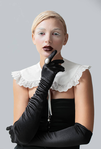 Beautiful young woman with creative makeup and elegant gloves on grey background - Photo, image