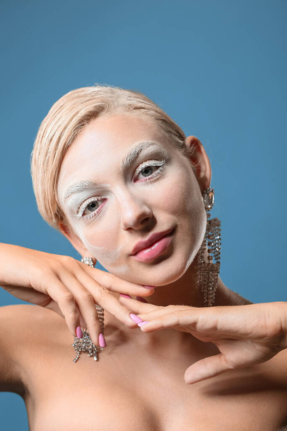 Schöne junge Frau mit kreativem Make-up und stilvollen Ohrringen auf farbigem Hintergrund - Foto, Bild