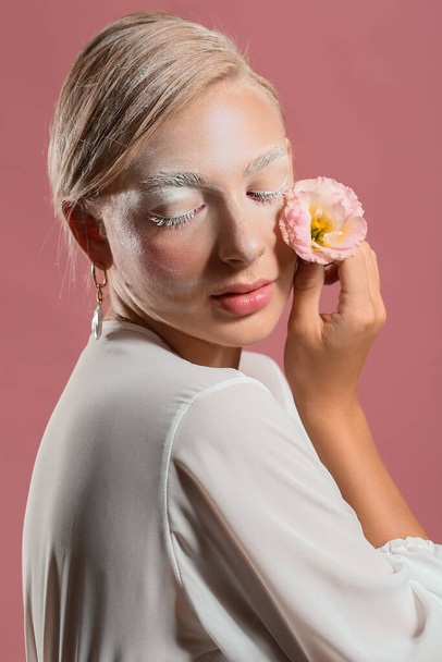 Beautiful young woman with creative makeup and eustoma flower on color background - 写真・画像