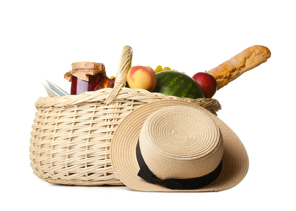Proutěný koš s chutným jídlem na piknik a klobouk na bílém pozadí - Fotografie, Obrázek