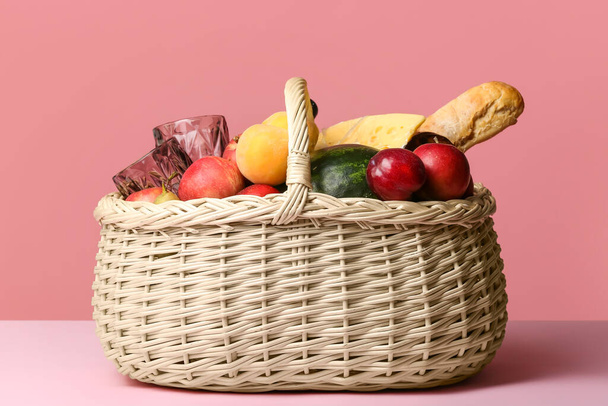 Cesta de mimbre con sabrosa comida para picnic sobre fondo de color - Foto, imagen