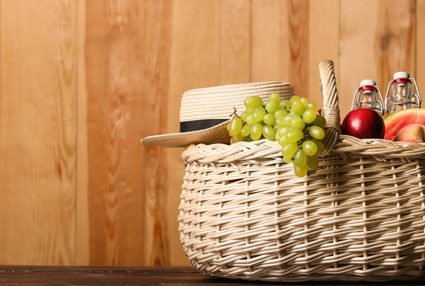 Wicker basket with tasty food, drink for picnic and hat on wooden background - Photo, Image