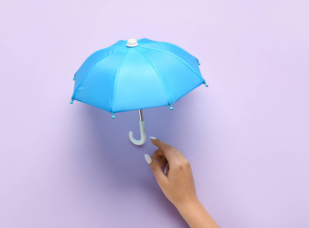 Female hand with mini umbrella on lilac background, closeup - Фото, изображение