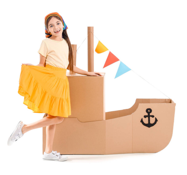 Αστείο κοριτσάκι που παίζει με χαρτονένιο πλοίο σε λευκό φόντο - Φωτογραφία, εικόνα