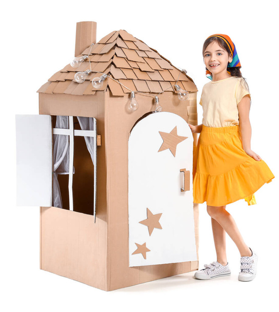 Забавная маленькая девочка играет с картонным домиком на белом фоне - Фото, изображение