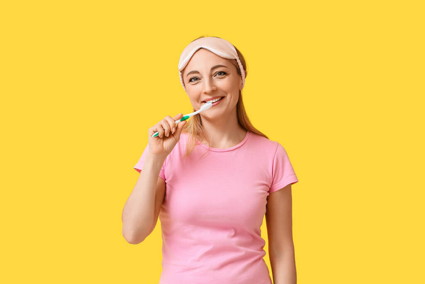 Όμορφη ώριμη γυναίκα βούρτσισμα δοντιών σε κίτρινο φόντο - Φωτογραφία, εικόνα