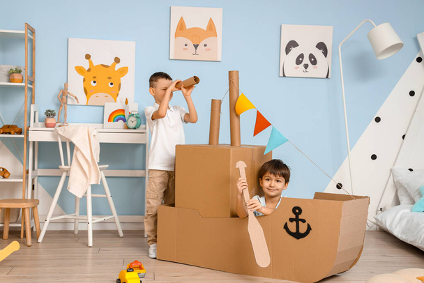 Vtipní malí kluci hrající si doma s lepenkovou lodí - Fotografie, Obrázek