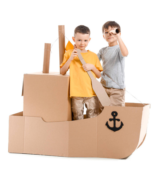 Funny little boys playing with cardboard ship on white background - Fotoğraf, Görsel