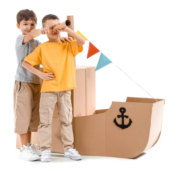 Lustige kleine Jungen spielen mit Pappschiff auf weißem Hintergrund - Foto, Bild