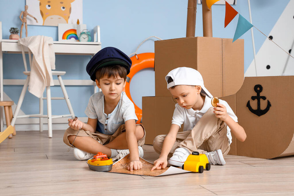 Vtipní malí kluci si hrají s kartonovou lodí a mapou doma - Fotografie, Obrázek