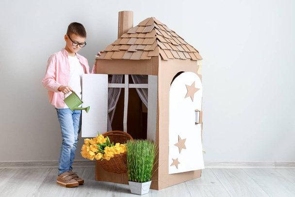 Забавный маленький мальчик играет с картонным домиком на светлом фоне - Фото, изображение