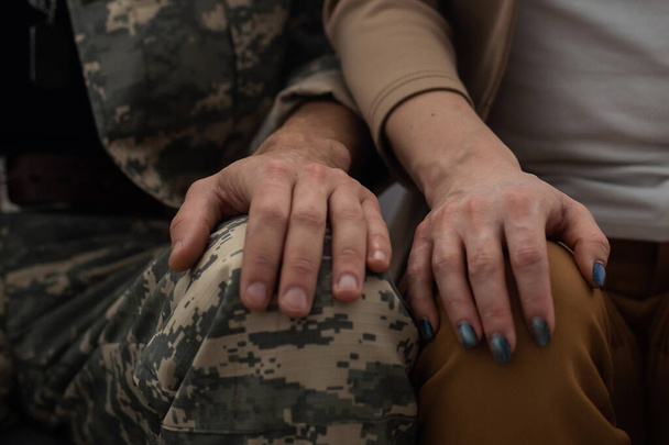 Close-up van mannelijke en vrouwelijke handen die elkaar zachtjes vasthouden. Een soldaat in militair uniform die de hand van een vrouw, zijn vriendin of vrouw neemt. Happy meeting concept. - Foto, afbeelding
