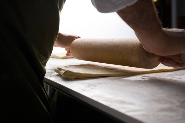 cook rolls out the dough with a rolling pin in the kitchen - Valokuva, kuva