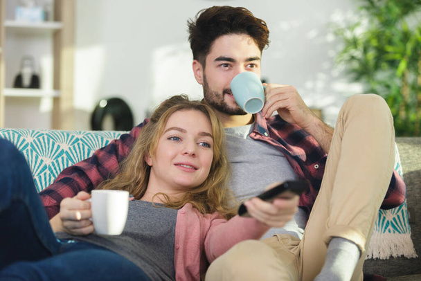 young couple sitting on sofa with cups of tea - Foto, imagen