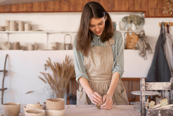 Maître de la céramique d'art au travail femme heureuse dans un tablier travaille dans un atelier de céramique. L'artisan crée des plats faits à la main dans l'atelier. Concept de compétence et d'entrepreneuriat - Photo, image