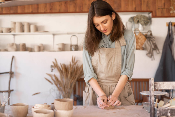 Maestro di ceramica d'arte al lavoro donna felice in un grembiule lavora in un laboratorio di ceramica. L'artigiana crea piatti fatti a mano in laboratorio. Abilità e imprenditorialità concetto - Foto, immagini