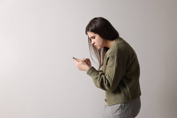 Young woman with bad posture using smartphone on grey background. Space for text - Fotoğraf, Görsel
