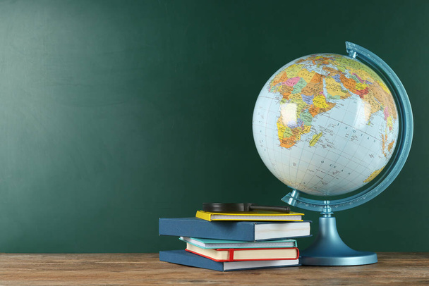 Globe, books and magnifying glass on wooden table near green chalkboard, space for text. Geography lesson - Фото, зображення