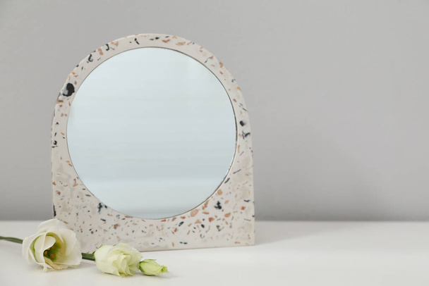 Stylish round mirror and flowers on table near white wall, space for text - Фото, зображення