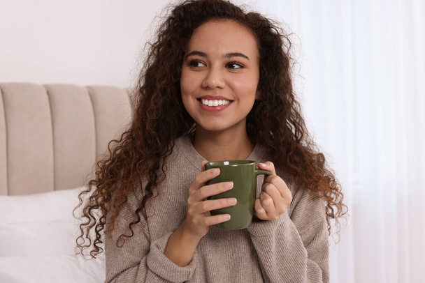 Happy African American woman with cup of drink in bedroom - Fotografie, Obrázek