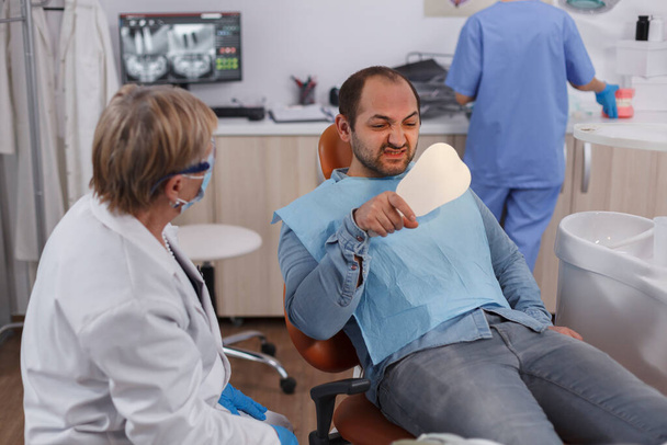 Пациент, держащий зеркало, смотрит на процедуру обработки зубов после операции - Фото, изображение