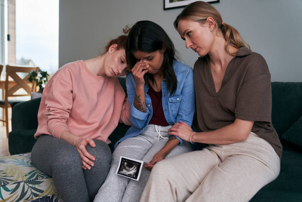 İki beyaz arkadaş tarafından teselli edilen ultrason taraması tutan melez bir kadın. - Fotoğraf, Görsel