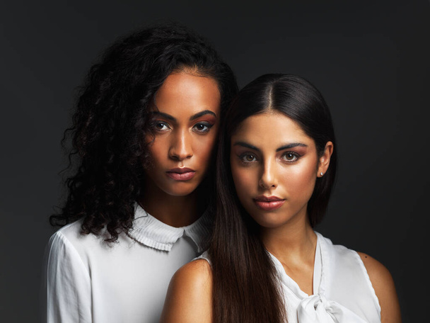 Women who support each other can conquer the world. Portrait of two attractive young women wearing white blouses posing closely together against a dark background in the studio. - Foto, Imagem