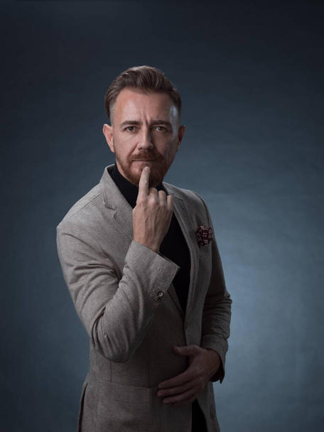 Portrait of a stylish elegant senior businessman with a beard and casual business clothes in photo studio isolated on dark background gesturing with hands - Foto, Imagen