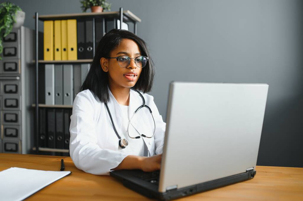 Smiling young adult indian female doctor wear white coat in medical clinic office. Happy beautiful health care india professional medic physician, therapist, headshot portrait. - Foto, imagen