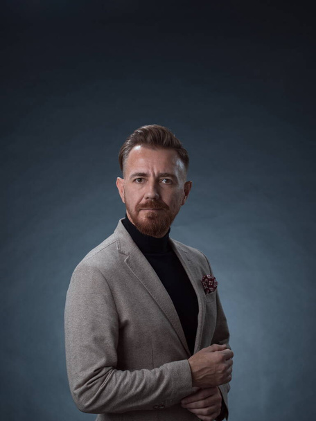 Portrait of a stylish elegant senior businessman with a beard and casual business clothes in photo studio isolated on dark background gesturing with hands - Fotó, kép