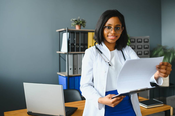 Smiling young adult indian female doctor wear white coat in medical clinic office. Happy beautiful health care india professional medic physician, therapist, headshot portrait. - 写真・画像
