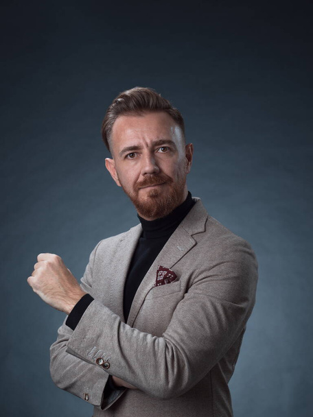 Portrait of a stylish elegant senior businessman with a beard and casual business clothes in photo studio isolated on dark background gesturing with hands - Фото, зображення