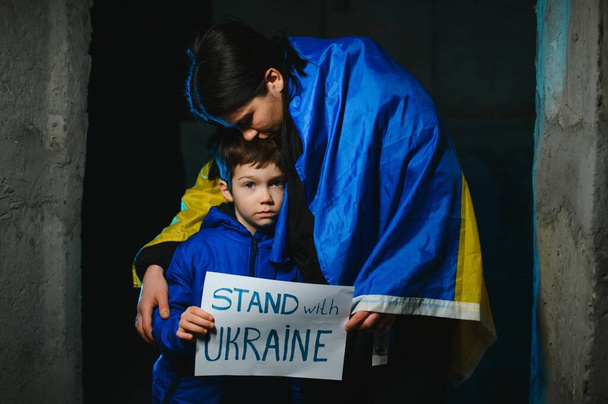 Sad mother hugging her son, both wearing Ukrainian national colors on black background. - Photo, Image