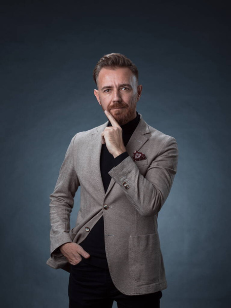 Portrait of a stylish elegant senior businessman with a beard and casual business clothes in photo studio isolated on dark background gesturing with hands - Foto, immagini