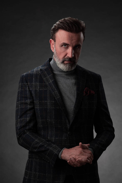 Portrait of a stylish elegant senior businessman with a beard and casual business clothes in photo studio isolated on dark background gesturing with hands - Foto, Bild