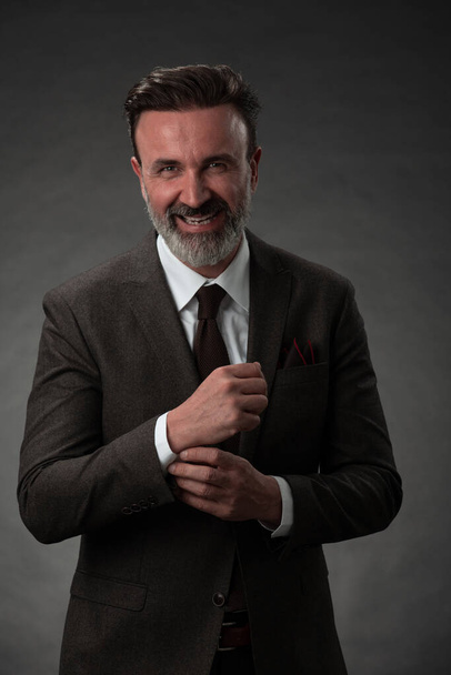 Portrait of a stylish elegant senior businessman with a beard and casual business clothes in photo studio adjusting suit - Fotografie, Obrázek