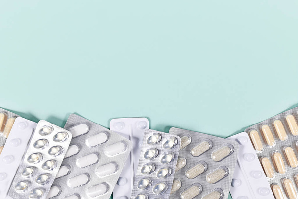 Blister packs with various pills and capsules at bottom of mint green background with copy space - 写真・画像